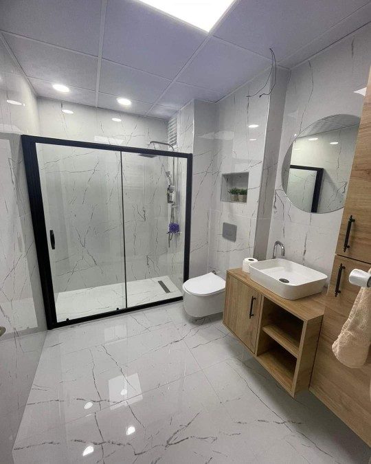 Banyo — mermer fayans, siyah çerçeveli duş ve ahşap lavabo