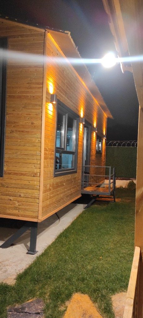 Ahşap tiny house — gece yan cephe ve metal giriş